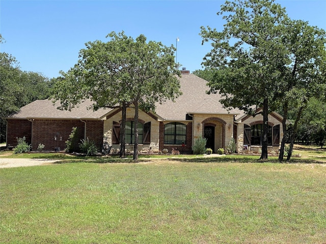 view of front of home featuring stone siding, brick siding, roof with shingles, and a front yard