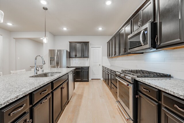 kitchen featuring a sink, light wood-style flooring, light stone counters, and stainless steel appliances