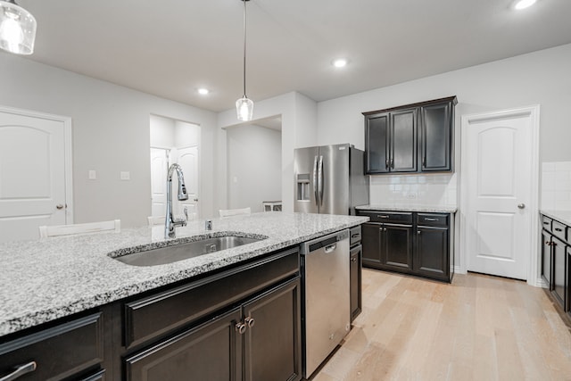 kitchen with light wood-style flooring, a sink, hanging light fixtures, stainless steel appliances, and tasteful backsplash