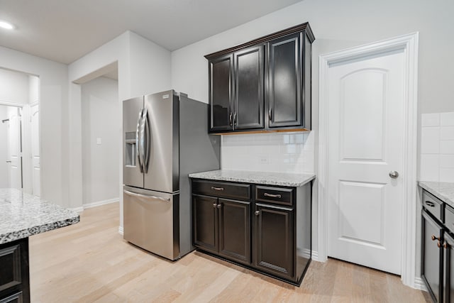 kitchen with light stone counters, backsplash, stainless steel fridge, light wood finished floors, and baseboards