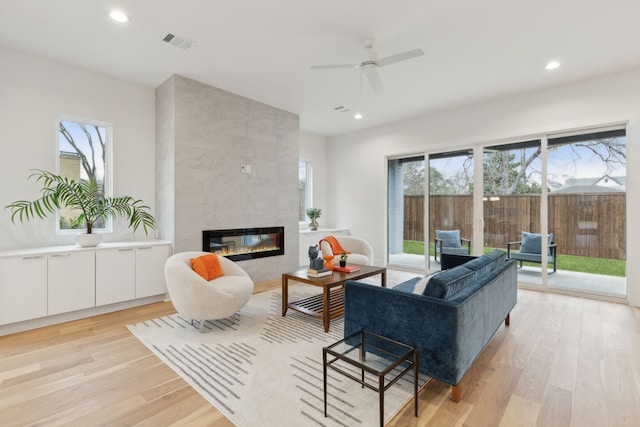 living room featuring a tiled fireplace, visible vents, recessed lighting, and light wood finished floors