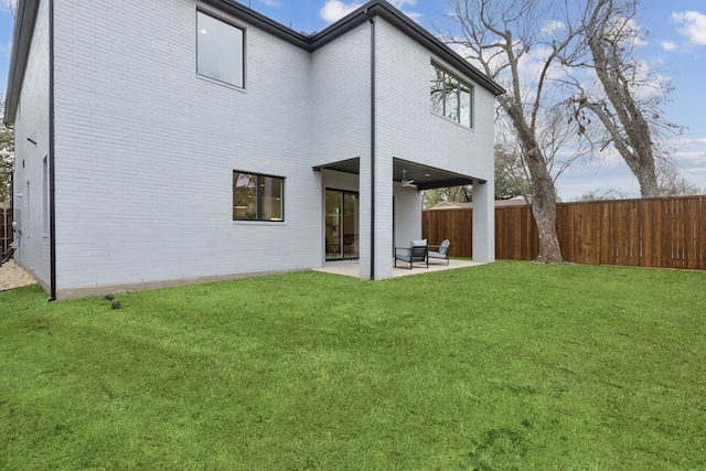 rear view of house featuring brick siding, a lawn, a patio, and fence