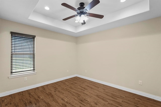 unfurnished room featuring a tray ceiling, wood finished floors, baseboards, and ceiling fan