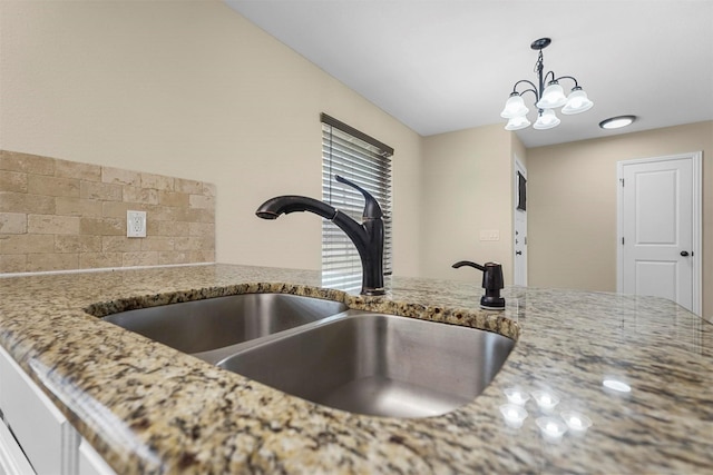 kitchen with decorative backsplash, decorative light fixtures, light stone countertops, and a sink