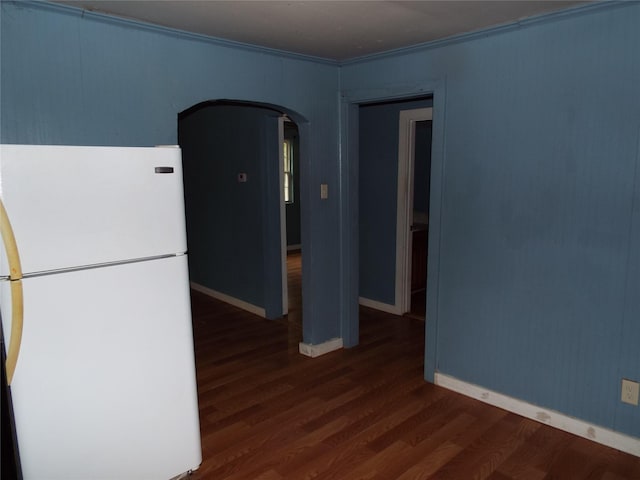 empty room with crown molding, wood finished floors, arched walkways, and baseboards