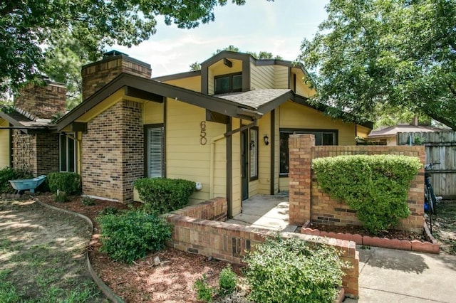 view of front of property with brick siding, a shingled roof, and fence