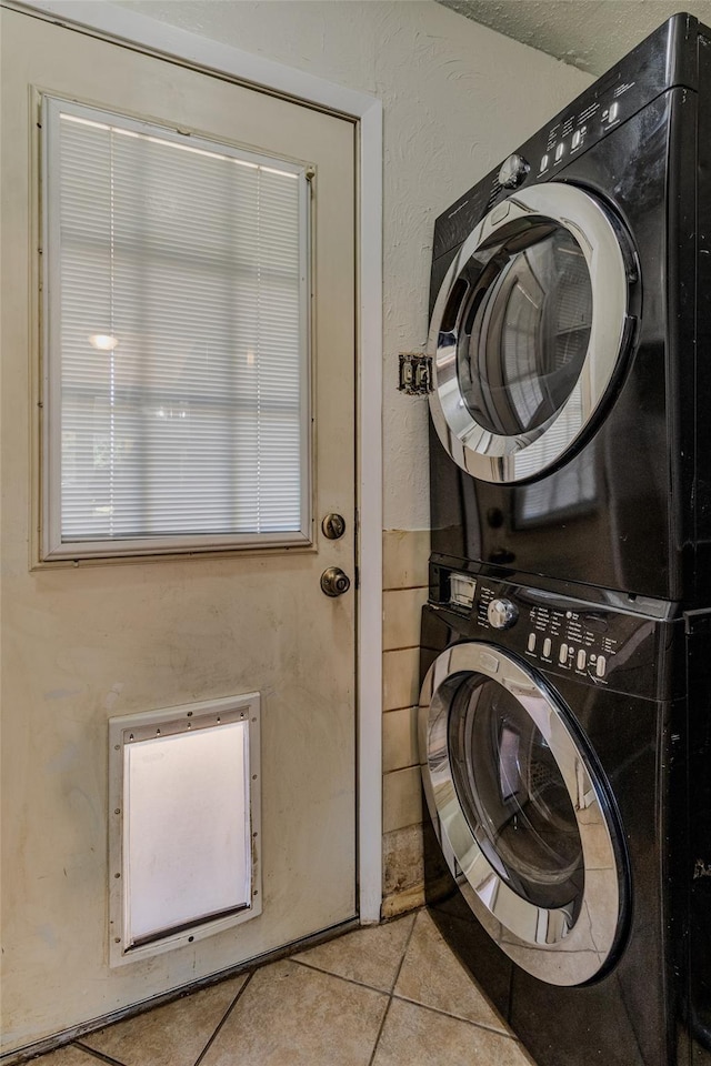 laundry area featuring laundry area, stacked washer and dryer, light tile patterned flooring, and a textured wall