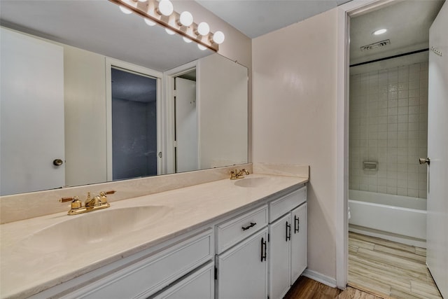 bathroom featuring visible vents, a sink, wood finished floors, double vanity, and baseboards