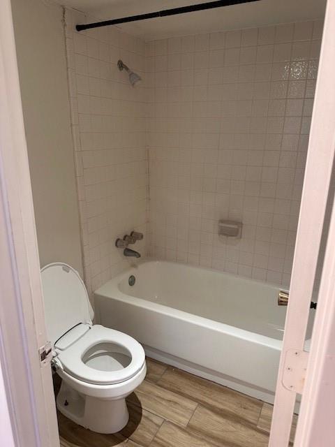 bathroom with bathing tub / shower combination, toilet, and wood finished floors