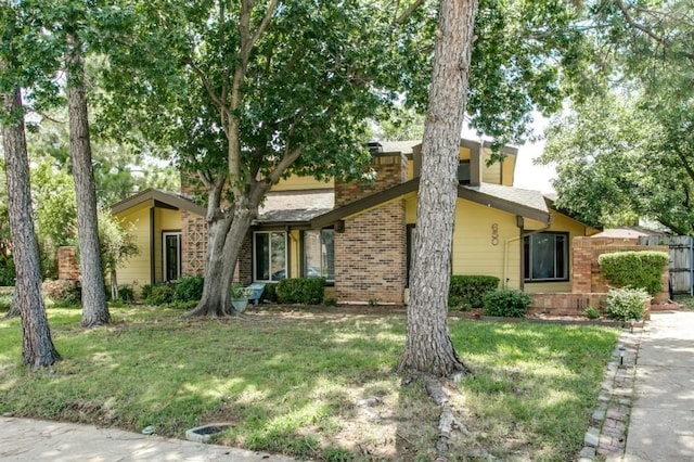 view of front facade with brick siding, a front lawn, and fence