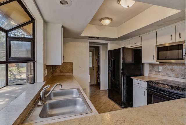 kitchen featuring black appliances, a sink, white cabinets, decorative backsplash, and a raised ceiling