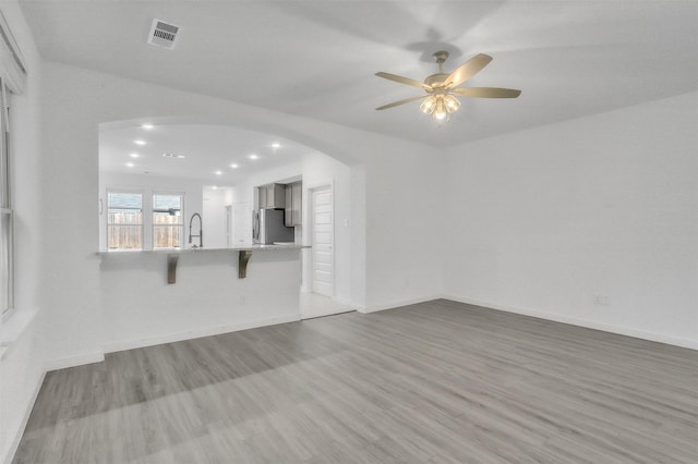 unfurnished living room featuring wood finished floors, visible vents, arched walkways, and baseboards