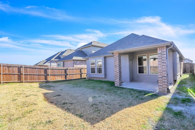 rear view of property with a patio, a fenced backyard, a yard, a shingled roof, and brick siding