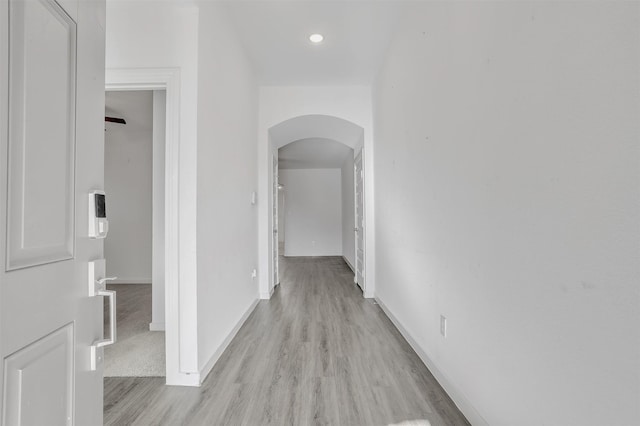 corridor featuring baseboards, arched walkways, and light wood-type flooring