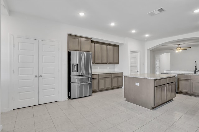 kitchen with visible vents, stainless steel refrigerator with ice dispenser, a sink, light stone counters, and arched walkways