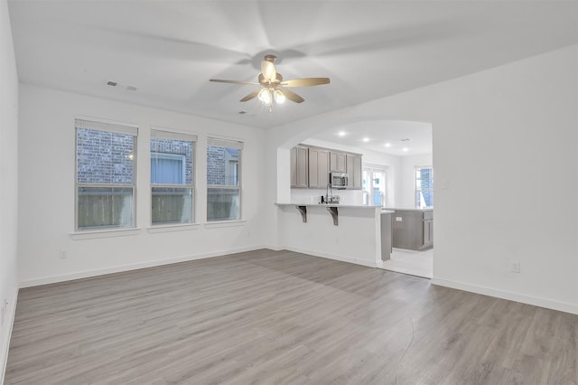 unfurnished living room with baseboards, visible vents, arched walkways, ceiling fan, and light wood-type flooring