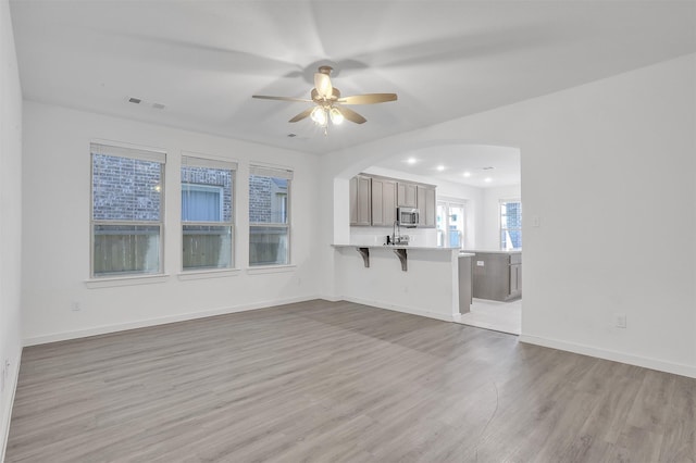 3917 Spencer Ln, Heartland, TX 75126 - unfurnished living room featuring light wood-style floors, a ceiling fan, arched walkways, and baseboards