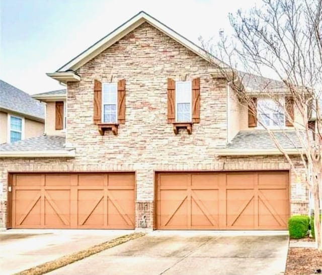 townhome / multi-family property with an attached garage, brick siding, driveway, and roof with shingles