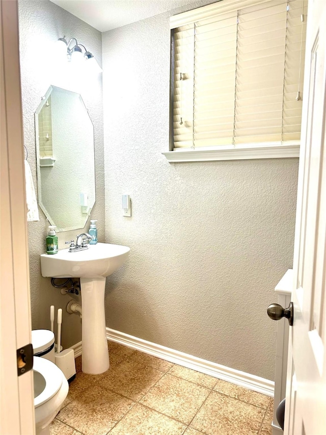 half bath with toilet, a textured wall, and baseboards