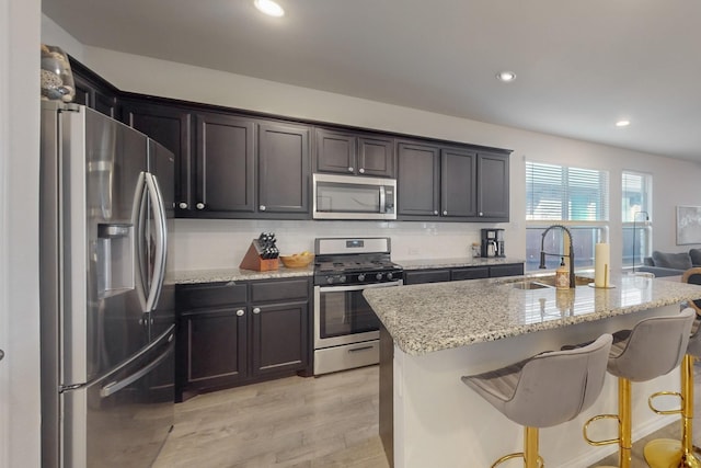 kitchen featuring a sink, backsplash, stainless steel appliances, light wood finished floors, and light stone countertops