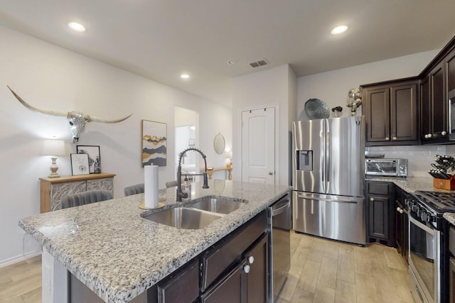 kitchen featuring visible vents, light wood-style flooring, a sink, stainless steel appliances, and light stone countertops