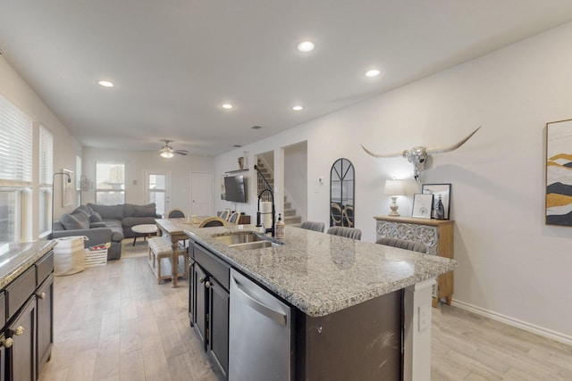 kitchen featuring a center island with sink, a sink, open floor plan, stainless steel dishwasher, and light wood-type flooring