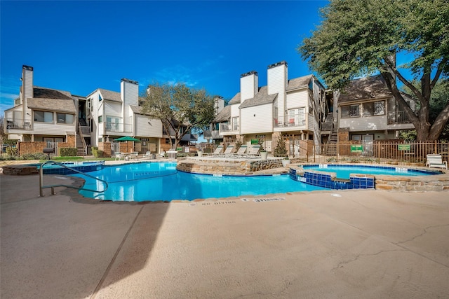 view of pool featuring a patio, fence, a residential view, and a pool with connected hot tub