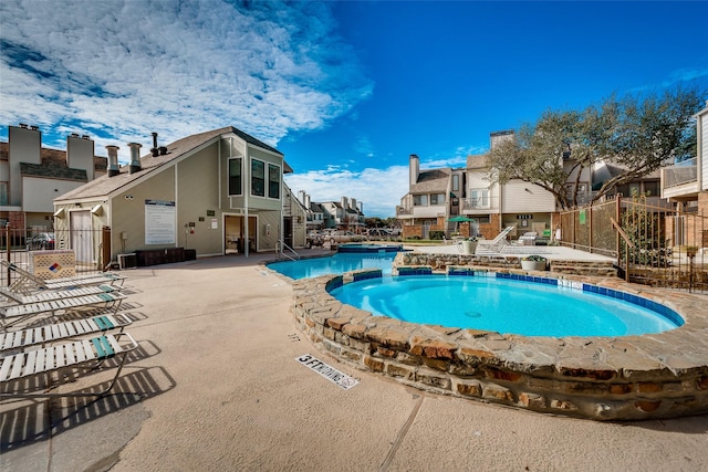 view of swimming pool featuring a patio, fence, a residential view, and a pool with connected hot tub