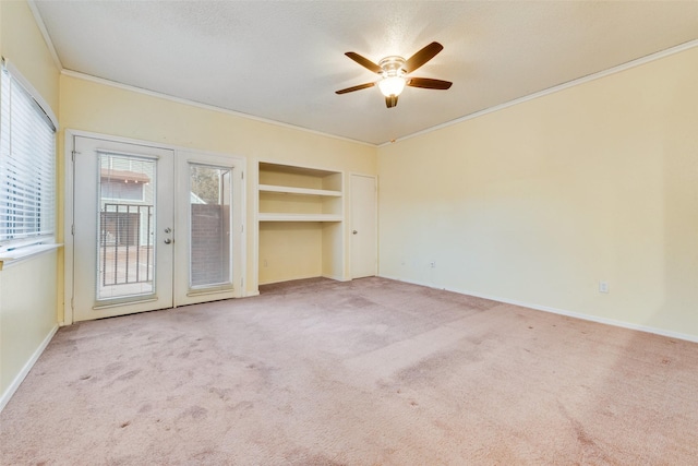 empty room featuring ornamental molding, built in features, french doors, carpet flooring, and baseboards