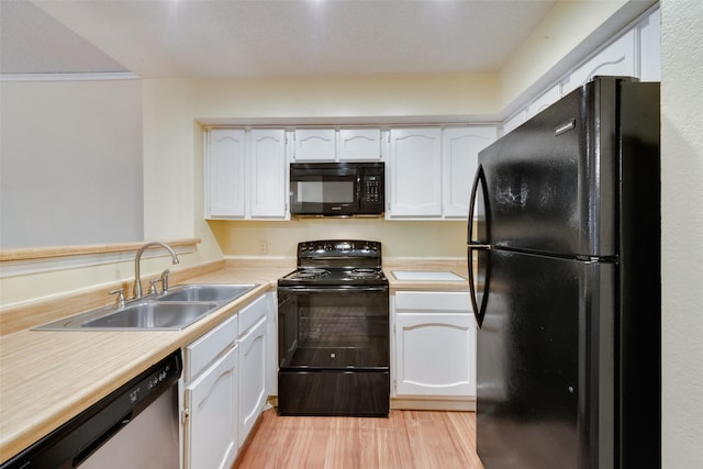 kitchen with a sink, light wood-style flooring, black appliances, and white cabinets