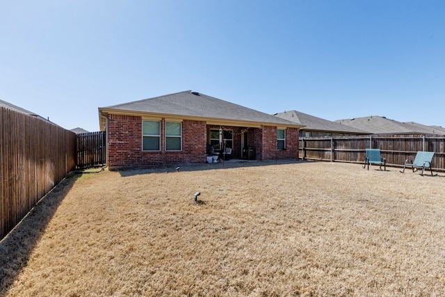 back of property with brick siding, a lawn, a shingled roof, and a fenced backyard