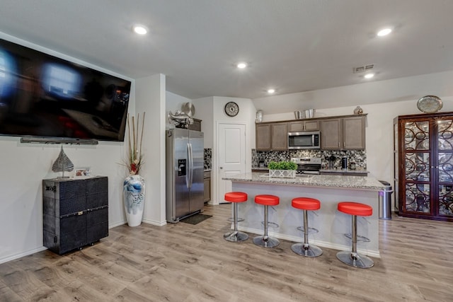 kitchen featuring visible vents, a kitchen bar, light wood-type flooring, decorative backsplash, and stainless steel appliances