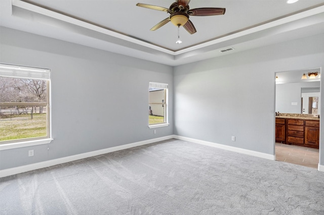 unfurnished bedroom featuring a tray ceiling, multiple windows, light colored carpet, and visible vents