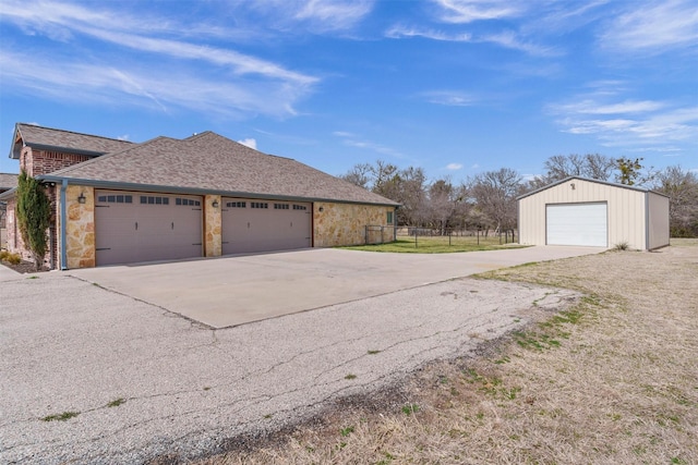 view of home's exterior with stone siding, fence, roof with shingles, an outdoor structure, and a garage