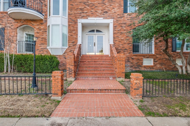 doorway to property with brick siding, french doors, and fence