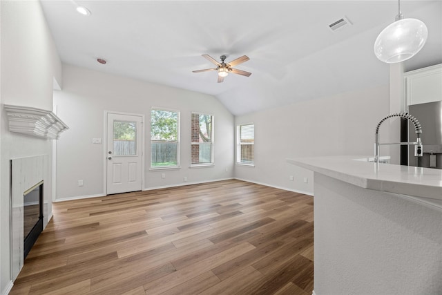 unfurnished living room featuring a ceiling fan, baseboards, visible vents, a tiled fireplace, and light wood-type flooring