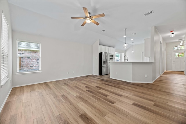 unfurnished living room featuring plenty of natural light, light wood-style flooring, a ceiling fan, and visible vents