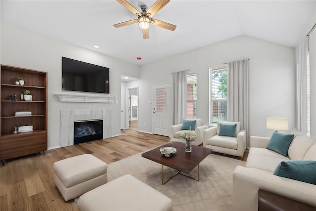 living room featuring light wood-style floors, a glass covered fireplace, a ceiling fan, and vaulted ceiling