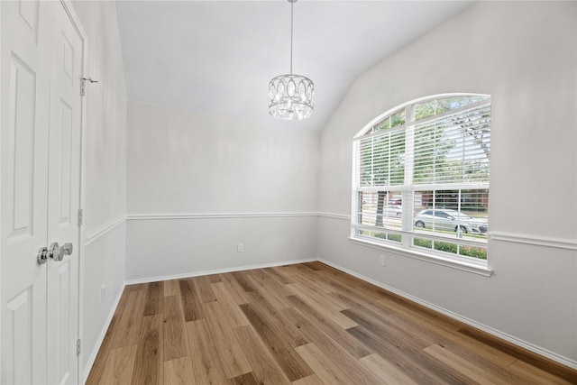 empty room with baseboards, a notable chandelier, wood finished floors, and vaulted ceiling