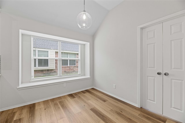 empty room with vaulted ceiling, baseboards, and light wood-type flooring