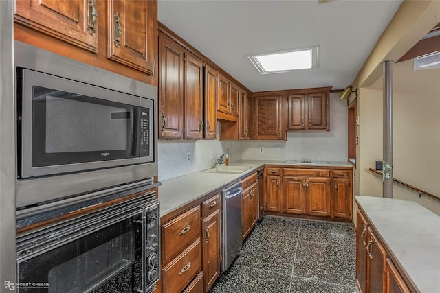 kitchen featuring brown cabinetry, granite finish floor, a sink, light countertops, and appliances with stainless steel finishes