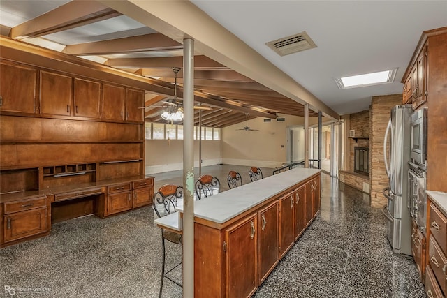 kitchen featuring visible vents, a ceiling fan, granite finish floor, stainless steel appliances, and a fireplace