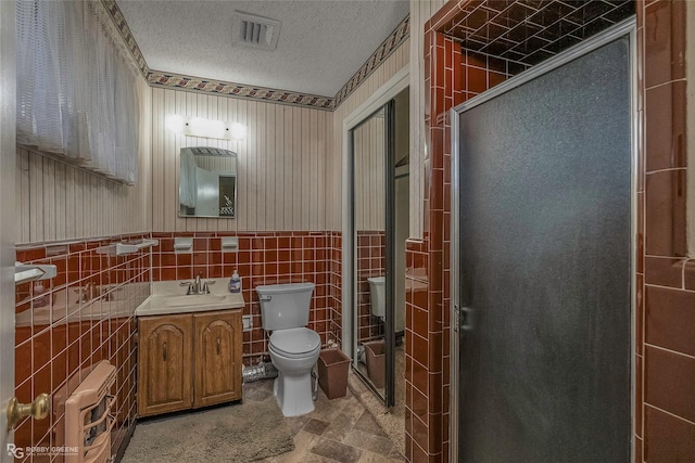 full bath with a wainscoted wall, toilet, heating unit, a textured ceiling, and tile walls