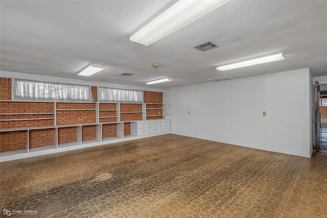 empty room featuring tile patterned floors, visible vents, brick wall, and a textured ceiling