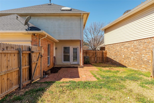 back of property featuring brick siding, fence private yard, roof with shingles, a yard, and a patio area