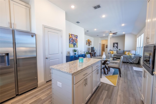 kitchen with light wood-type flooring, visible vents, a center island, appliances with stainless steel finishes, and light stone countertops