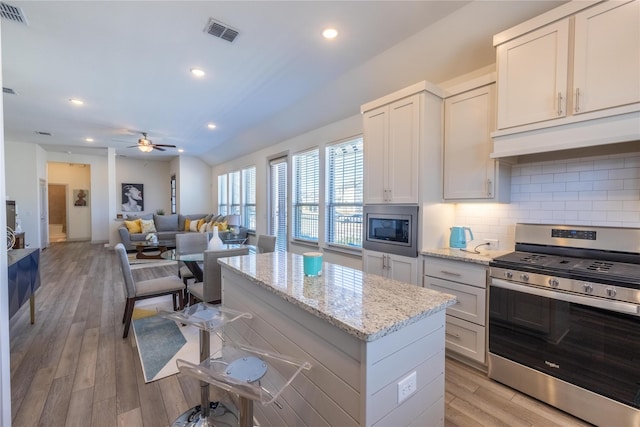 kitchen with visible vents, under cabinet range hood, a kitchen island, backsplash, and appliances with stainless steel finishes