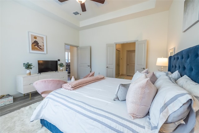 bedroom featuring visible vents, wood finished floors, a tray ceiling, and a towering ceiling