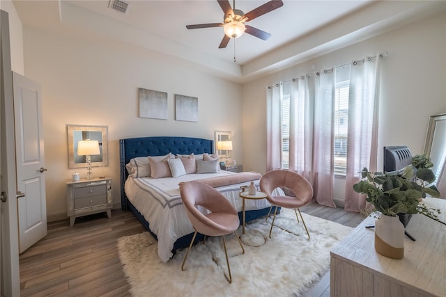 bedroom featuring a ceiling fan, a raised ceiling, wood finished floors, and visible vents