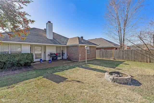 rear view of property with brick siding, a fire pit, fence, a yard, and a patio area